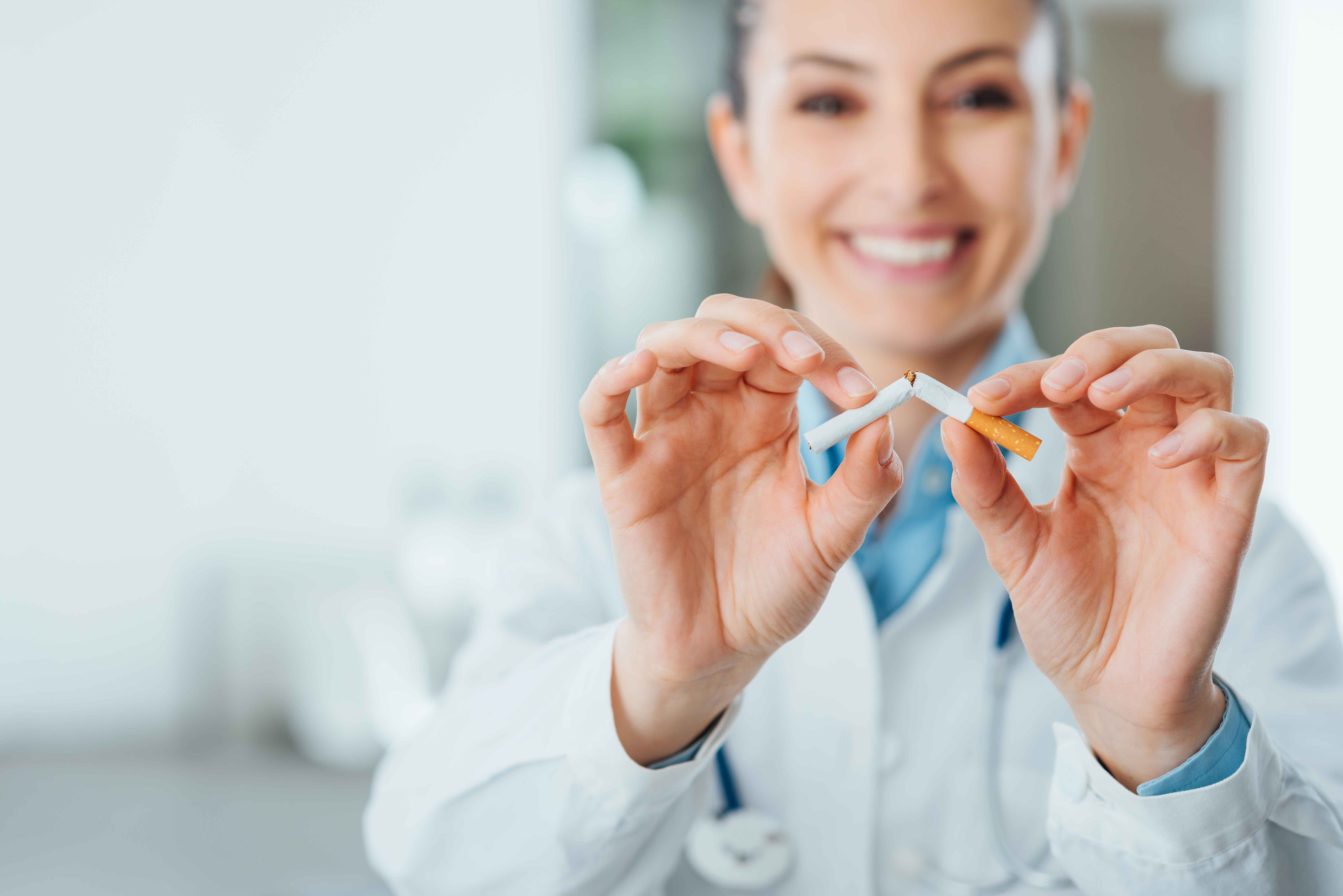 Das Foto zeigt eine Ärztin im weißen Kittel, die lächelnd eine Zigarette zerbricht.