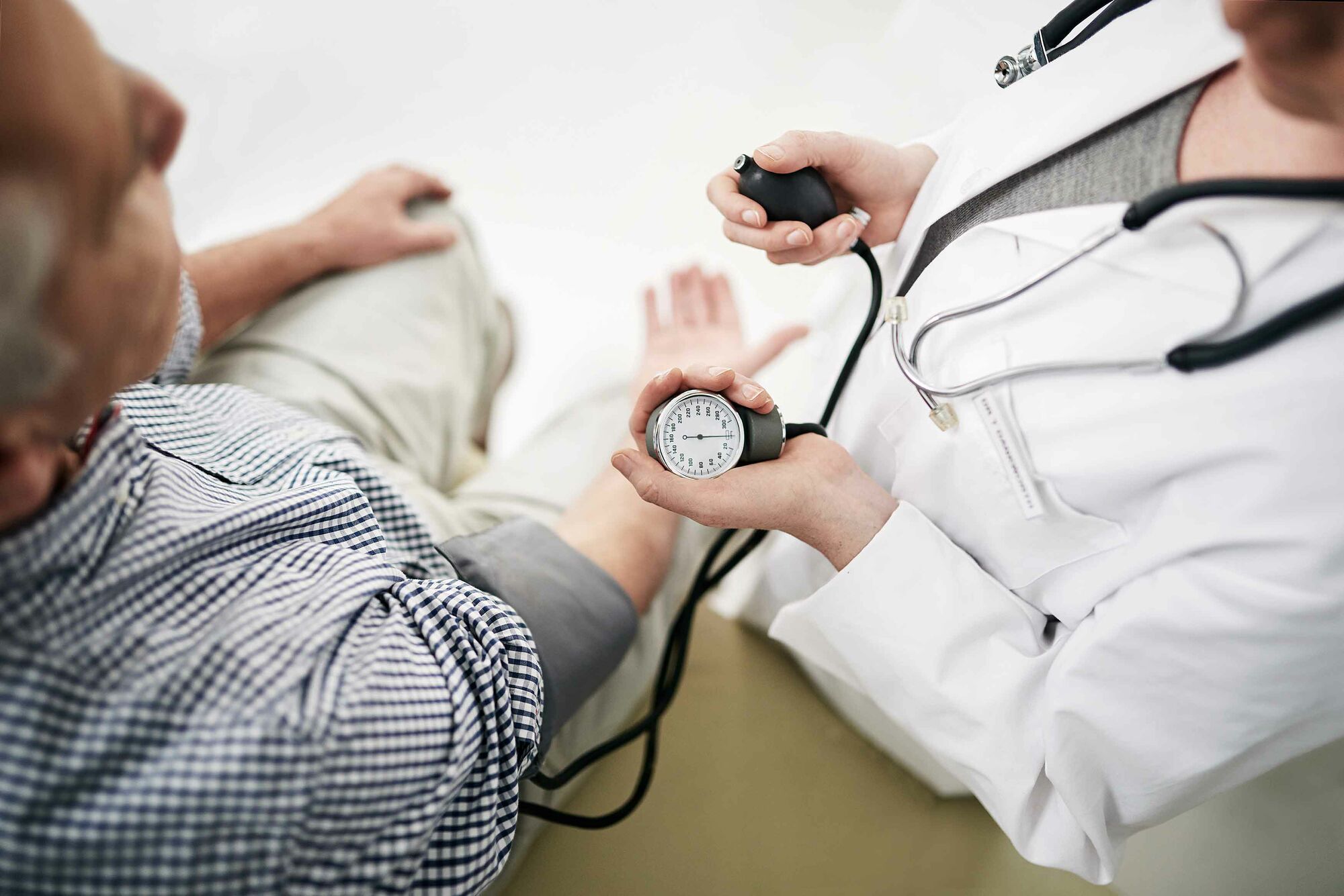 Das Foto zeigt eine Ärztin in weißem Kittel mit Stethoskop um den Hals, die einem älteren Herren den Blutdruck misst.