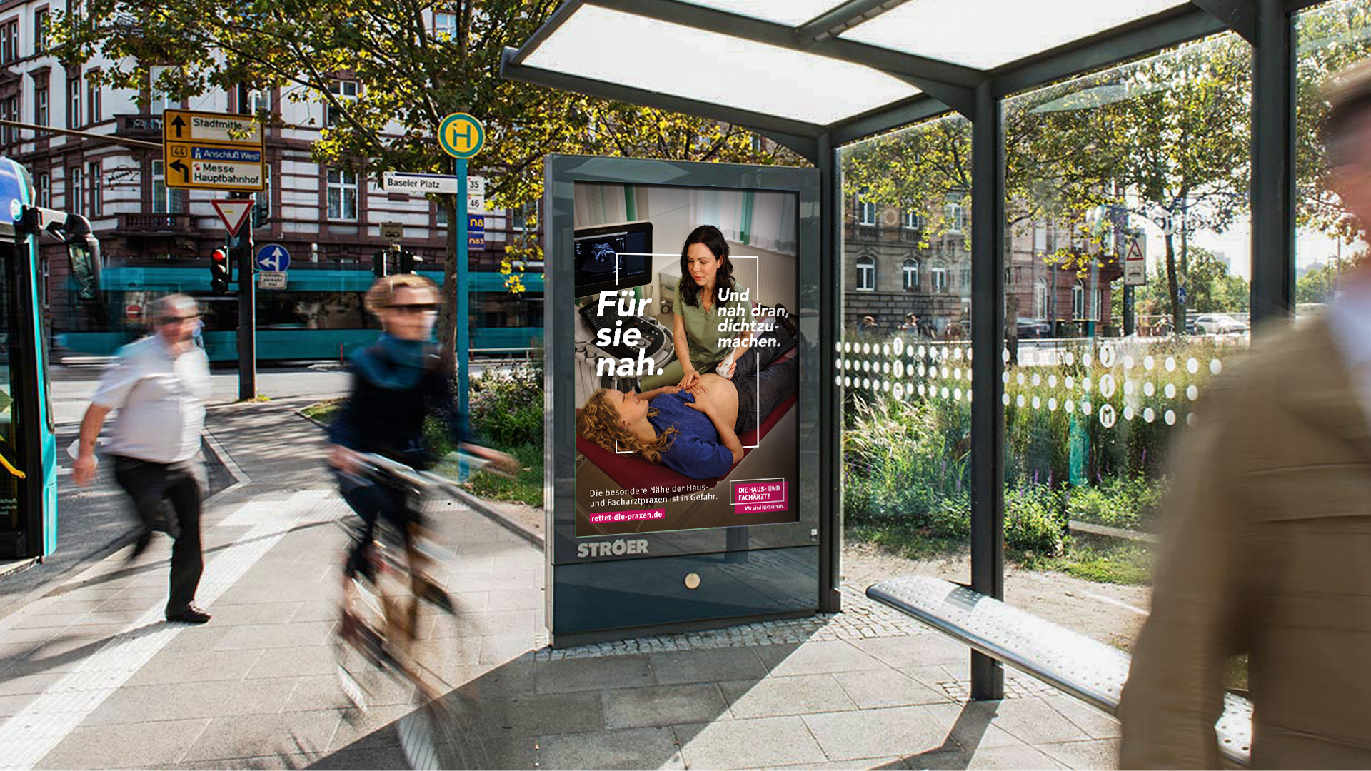 Foto von einer Bushaltestelle in einer belebenden Innenstadt - Menschen gehen und fahren an der Haltestelle vorbei - mit einem Citylight Poster von der neuen KBV Kampagne.
