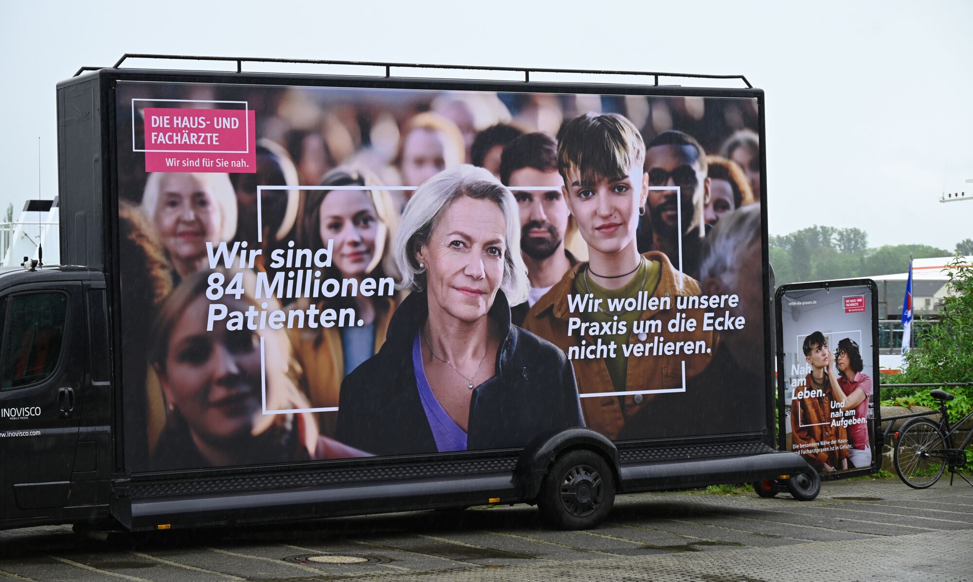Ein großes querformatiges und ein kleines Anzeigenmotiv der neuen KBV-Kampagne stehen an dem Ufer des Mainz